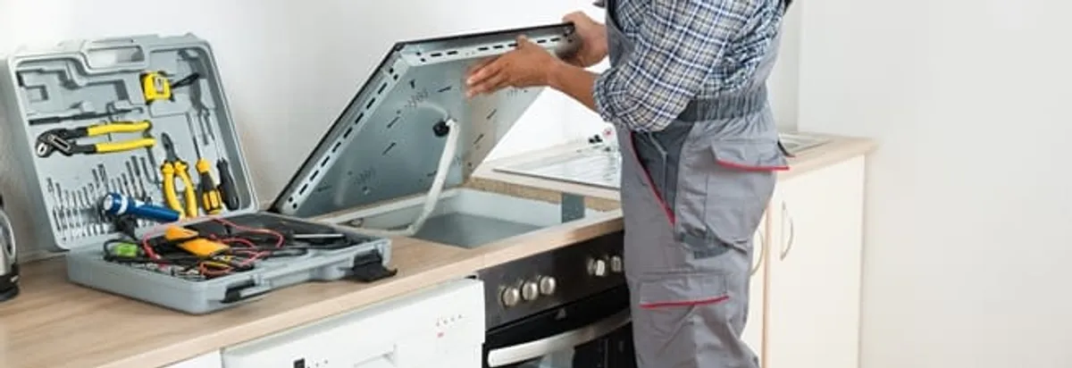 Cooktop repair technician lifting a built-in stovetop for service in Miami, FL